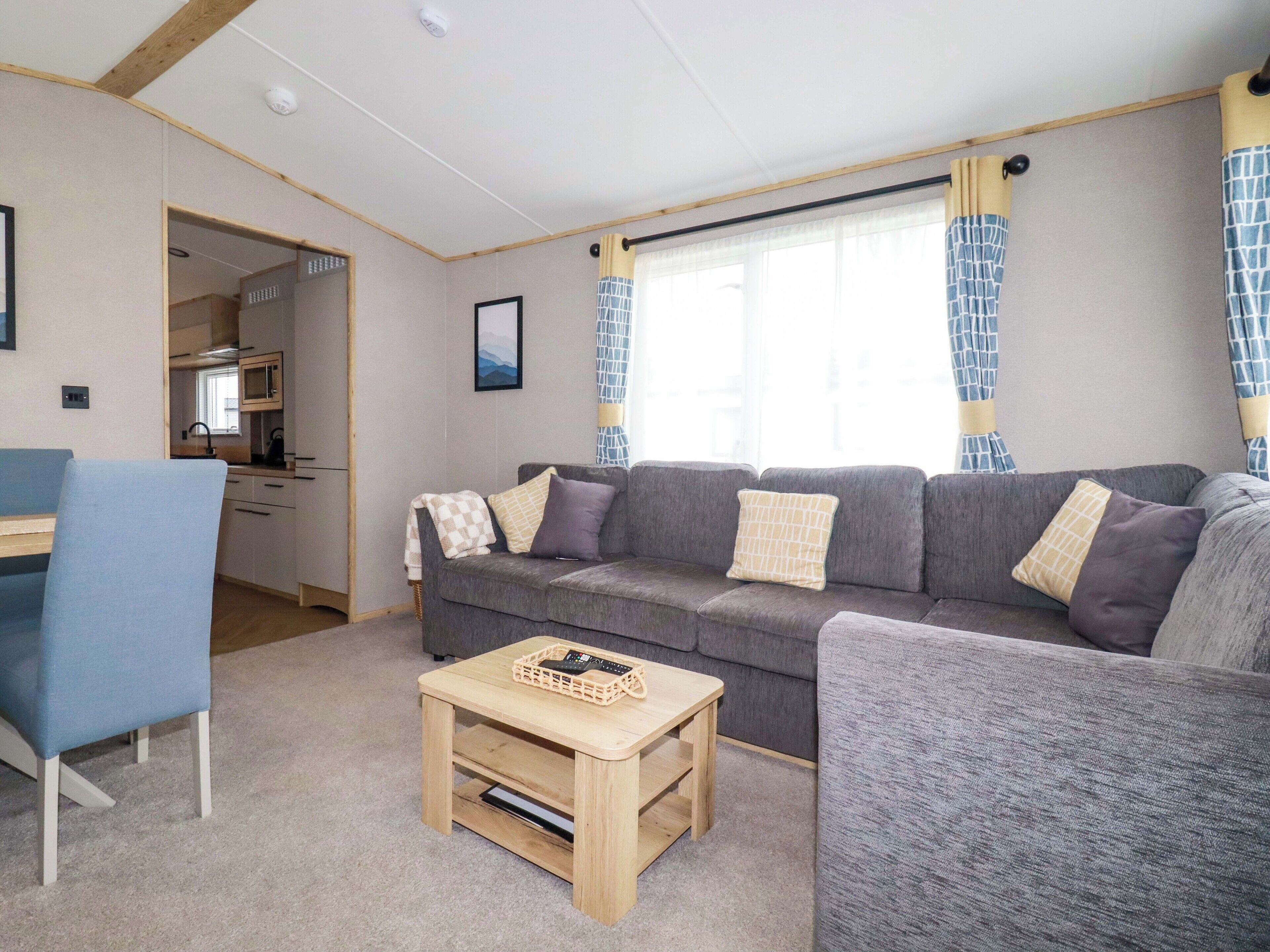 En kompakt opholdsstue med en sofa, et lille bord og en stol. Der er et tekøkken i baggrunden.