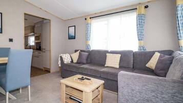 En kompakt opholdsstue med en sofa, et lille bord og en stol. Der er et tekøkken i baggrunden.
