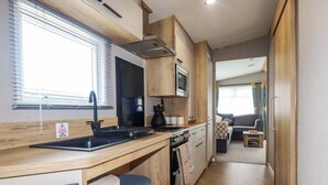 A compact kitchen with a sink, stove, and microwave. There is a small dining area with a table and chairs. - Coastal Escape (Par)