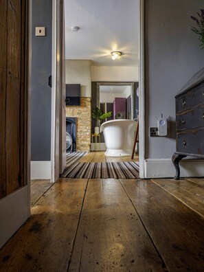 A wooden floor leading to a bathroom with a white bathtub, a mirror, and a wall-mounted light fixture. - 17th-Century Flint Cottage by Viking Bay (Kent)