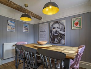 A dining area with a wooden table, chairs, and pendant lights. - 17th-Century Flint Cottage by Viking Bay (Kent)