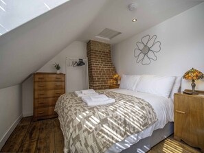 A bedroom with a bed, a wooden dresser, a brick fireplace, and a wall decoration. - 17th-Century Flint Cottage by Viking Bay (Kent)