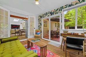 Ein geräumiges Wohnzimmer mit einem grünen Sofa, einem Holztisch und einem großen Fenster mit Blick ins Freie.