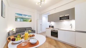 A modern kitchen with a microwave, oven, and sink. There's a dining table with fruits and a vase of flowers. - Cocon Meyerbeer 2 (Niza)