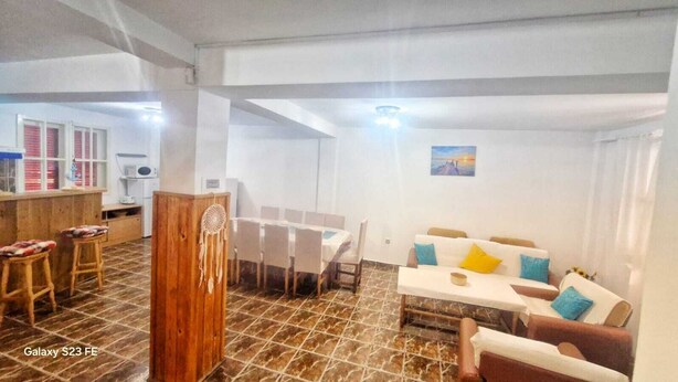 A spacious living area with a dining table, a sofa set, and a kitchen area with a bar. - Casa Cu Obloane Rosii By Cochilia (Eforie Nord)