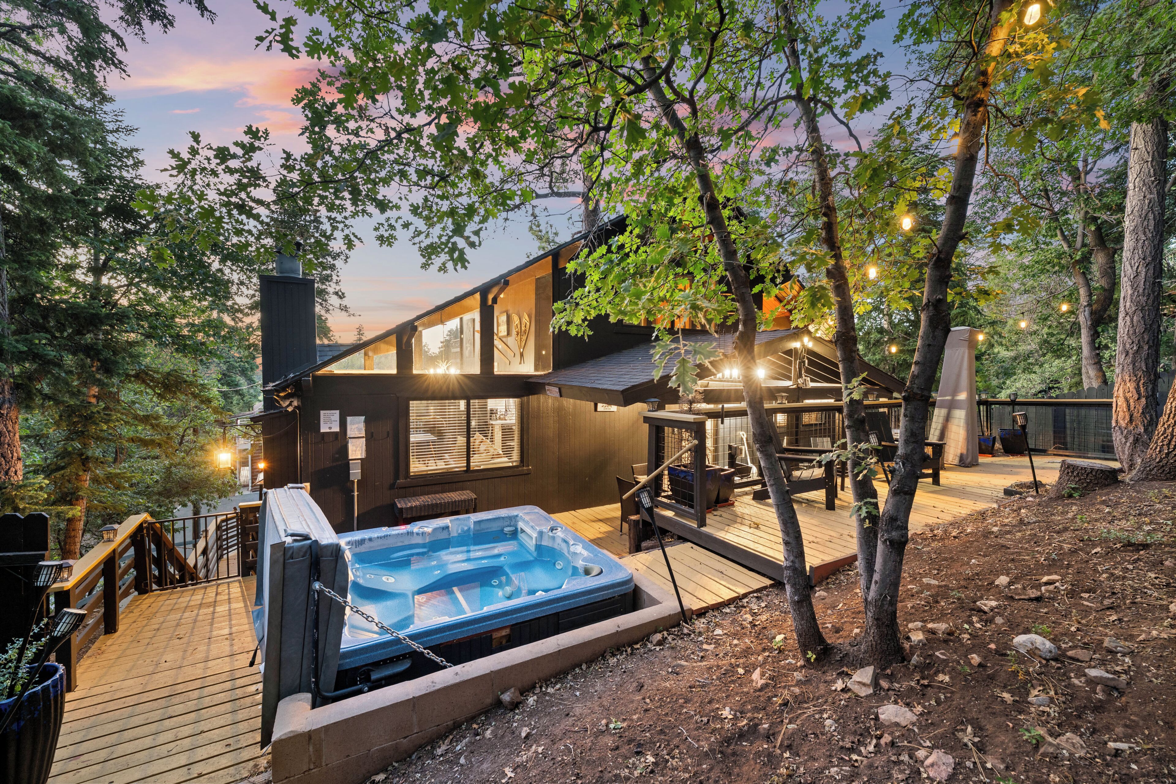 Een houten terras met een jacuzzi, omgeven door bomen en een gebouw met grote ramen.