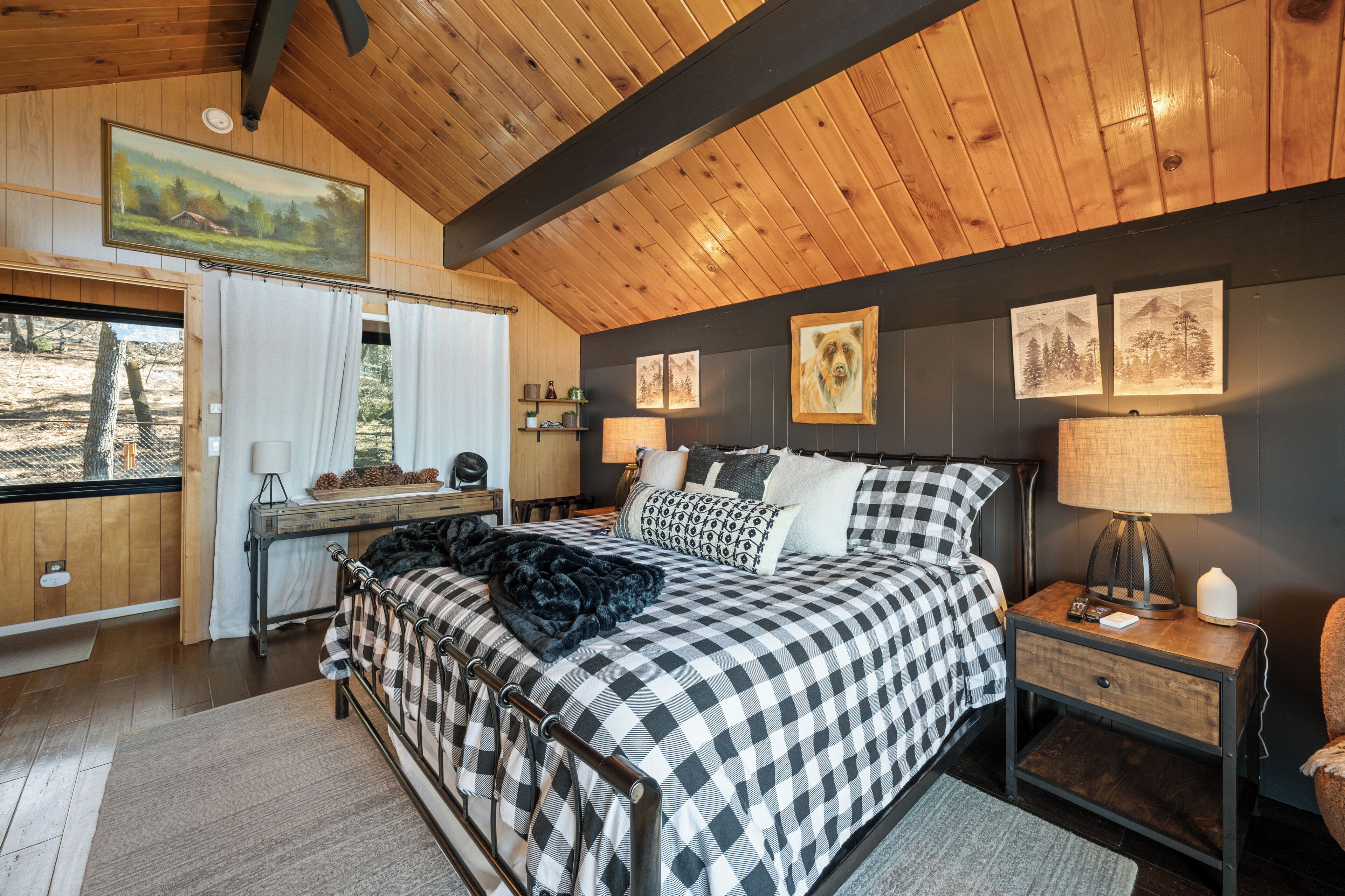A bedroom with a checkered bedspread, a wooden ceiling, and framed artwork on the walls.