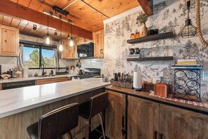 A kitchen with wooden cabinets, a large island with bar stools, a microwave, and a window with a view. - Chalet Steps to Bear Mountain, Hot Tub, King, Mountain Views, Fire Pit, AC (Big Bear Lake)