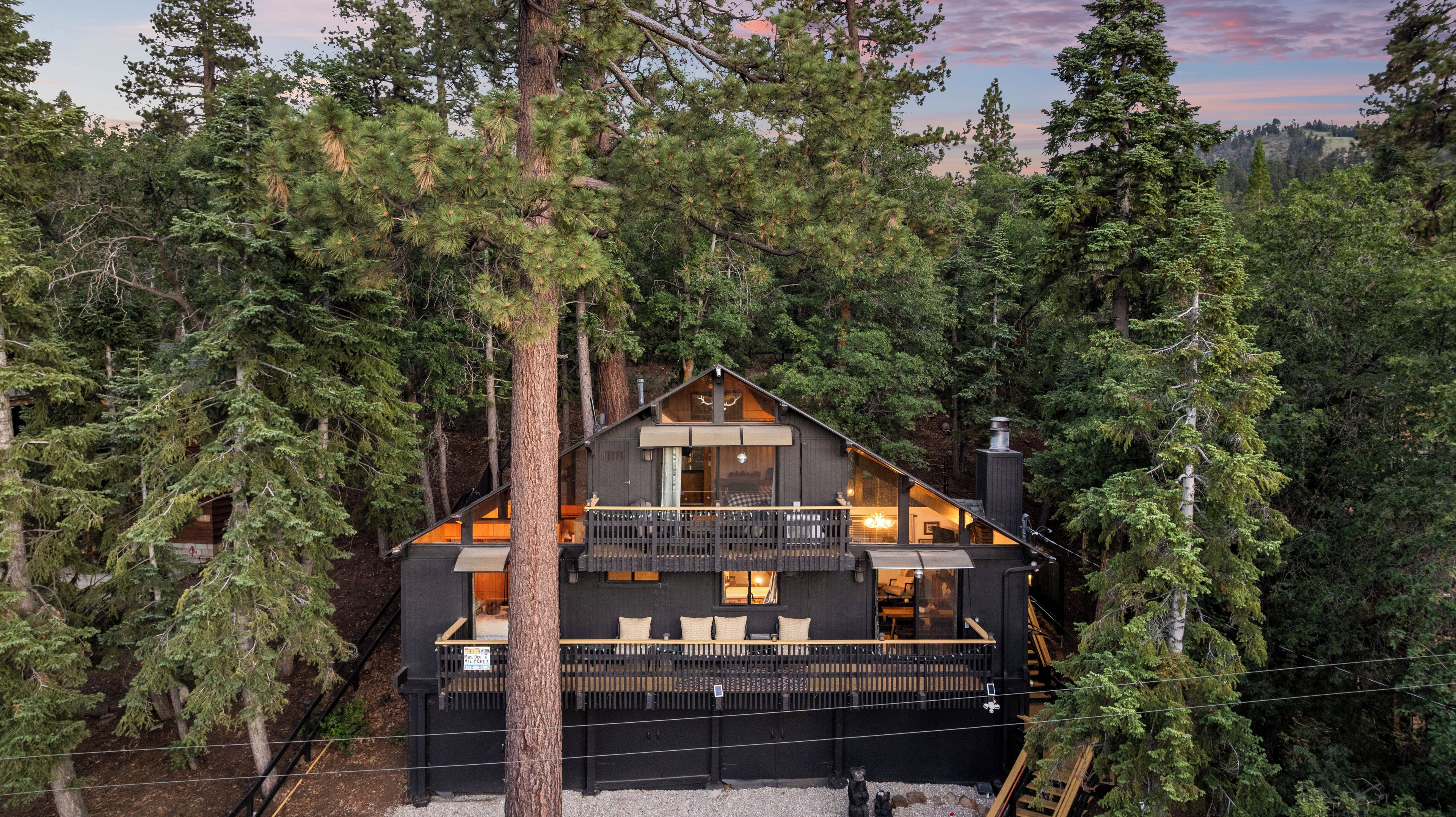 A cabin surrounded by tall trees, with a balcony and a chimney.
