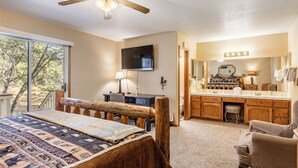 Ein Schlafzimmer mit Bett, Schreibtisch, Fernseher und einem Badezimmer mit Waschtisch sowie einem Deckenventilator.