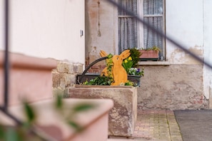 Una escultura de conejo de madera con flores, una jardinera de ladrillo y una ventana con cortinas estampadas.