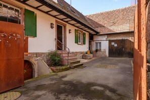 Un patio con una escalera que lleva a una puerta, un pequeño jardín y un edificio de ladrillo con techo de tejas.
