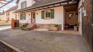 Ein zweistöckiges Haus mit überdachter Veranda, einem kleinen Garten und einer sichtbaren Treppe zum Eingang.