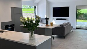 A modern kitchen with a central island, a dining area with a sofa, and a large TV. - The Studio @ Cherry Tree (Natland)