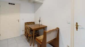 Een kamer met een houten eettafel, vier stoelen, een kleine vaas, een witte deur en een wit plafond met zichtbare balken.