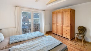 Een slaapkamer met twee bedden, een houten garderobe, een stoel en een balkon met uitzicht.