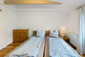 A bedroom with two single beds, a wooden wardrobe, a nightstand with a lamp, and a radiator. - Apartment with Castle View in the Heart of Wettin – Sleeps 2 Guests (Wettin-Löbejün)