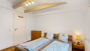 Een slaapkamer met twee enkele bedden, een houten garderobe, een nachtkastje met een lamp en een witte deur.