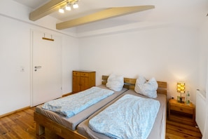A bedroom with two single beds, a wooden wardrobe, a nightstand with a lamp, and a white door.