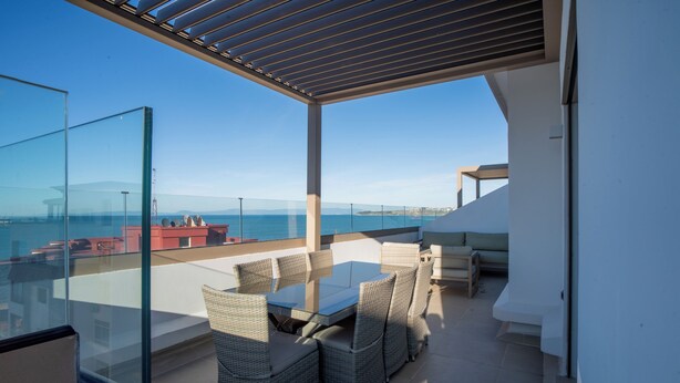 Een balkon met glazen omheining, tuinmeubilair en uitzicht op zee.