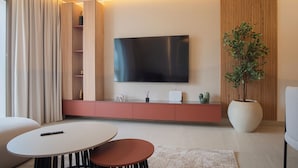 Een moderne woonkamer met een flatscreen televisie aan de muur, een grote potplant en een minimalistische meubilering.