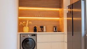 Een compacte keuken met een roestvrijstalen koelkast, een wasmachine en houten planken met ingebouwde verlichting.