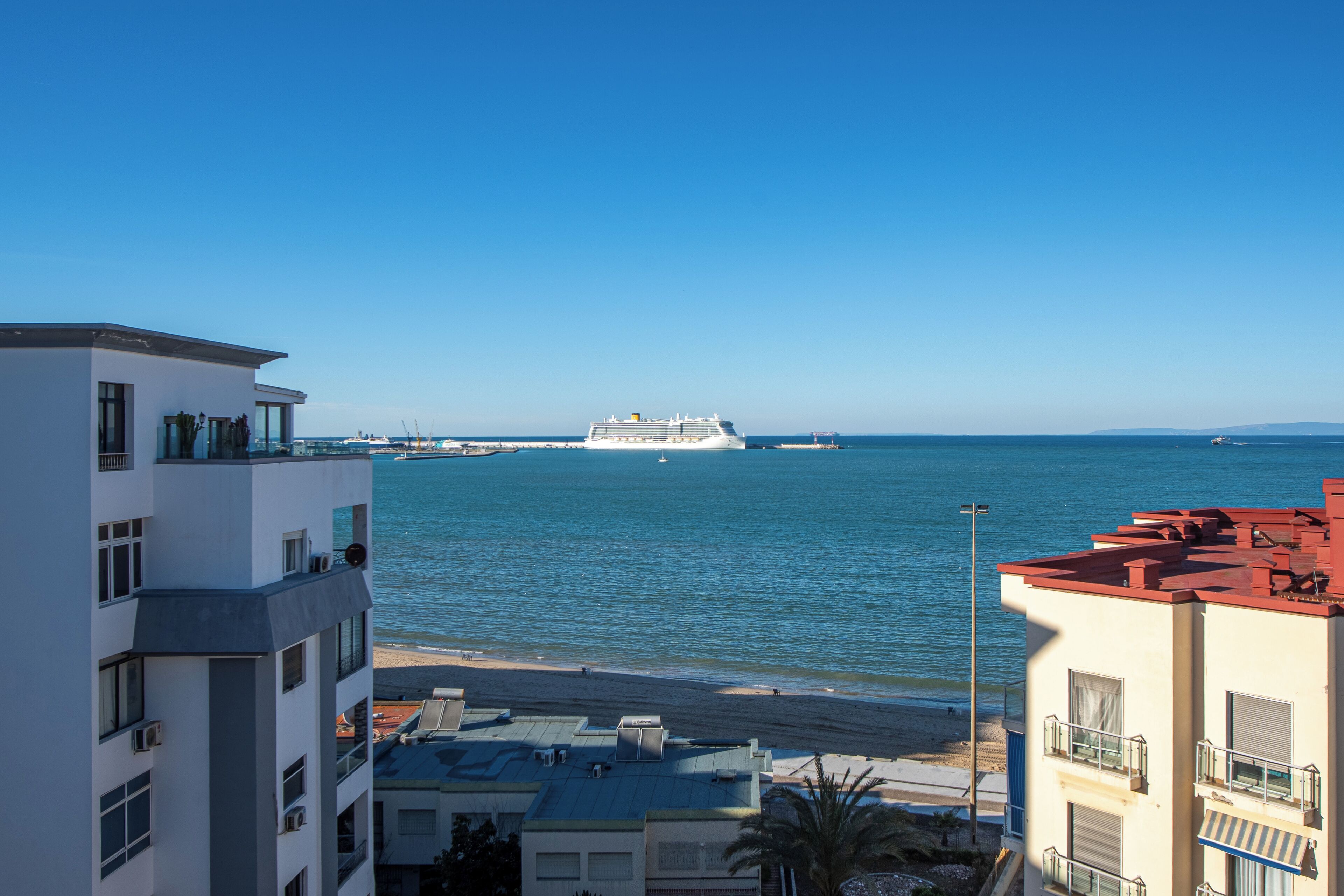A cruise ship in the distance, a beach, and buildings with balconies overlooking the sea.