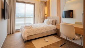 Ett modernt hotellrum med en stor säng, ett skrivbord, en stol, en TV och utsikt över staden.