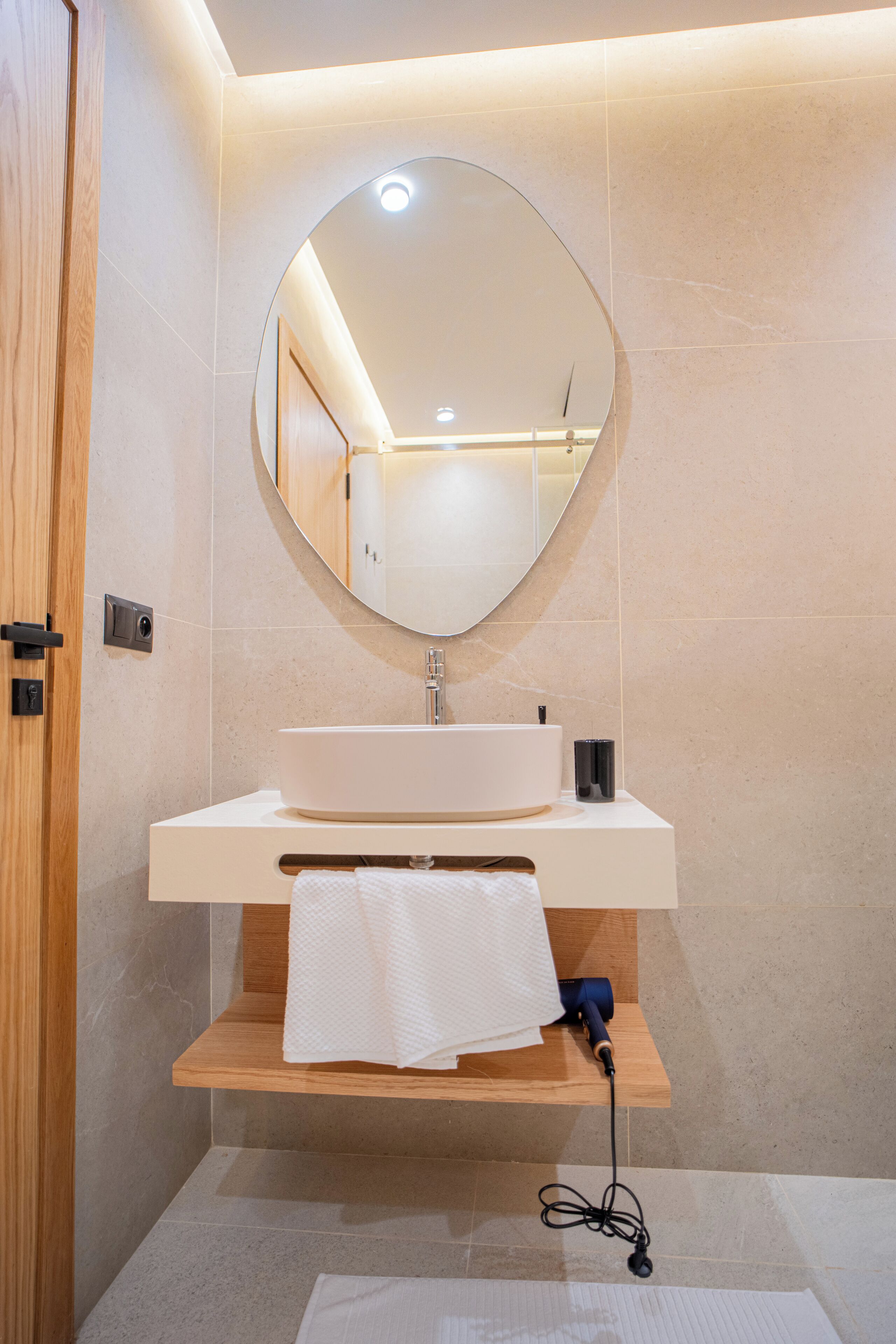 Une salle de bain moderne avec un miroir rond, un lavabo blanc et une étagère en bois.