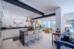 Eine moderne Küche mit Kochinsel, Barhocker, Pendelleuchten und einem großen Schiebeglastür, die auf eine Terrasse führt.