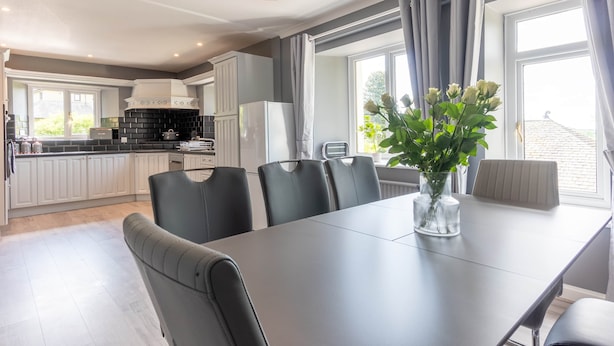 A modern kitchen with white cabinets, a black countertop, and a dining area with a table and chairs. - The House at Cherry Tree (Kendal)