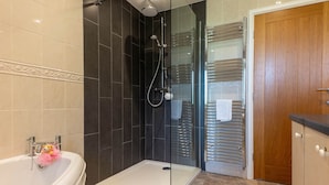 A modern bathroom with a glass shower enclosure, a white bathtub, and a wooden door. - The House at Cherry Tree (Kendal)