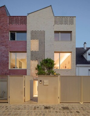 Ein modernes Wohngebäude mit Ziegelaußenwand, einem zentralen Bereich mit einer Lochwand und einer beigen Fassade.