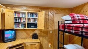 A bunk bed with a red and white checkered blanket, a wooden desk with a television, and a bookshelf filled with books and DVDs. - Trail and Tide-Sleeps 18- Hot tub and Game Room (Island Park)