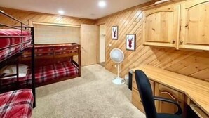 A bunk bed with plaid bedding, a desk with a chair, wooden cabinets, and a wall-mounted fan. - Trail and Tide-Sleeps 18- Hot tub and Game Room (Island Park)