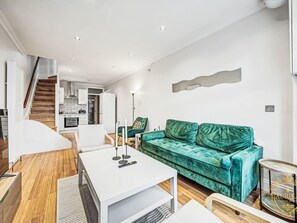 En moderne stue med en grøn sofa, et hvidt sofabord og en trappe, der fører op til et køkken.