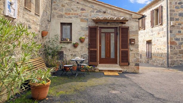 A stone building with a wooden door and shutters, a small outdoor seating area with a table and chairs, and potted plants. - Federico's Cantuccio, cozy apartment in the heart of Radicofani (Radicofani)