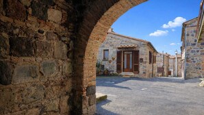 A stone building with a wooden door and shuttered windows, a paved street, and an archway. - Federico's Cantuccio, cozy apartment in the heart of Radicofani (Radicofani)