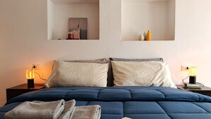 A bedroom with a large bed, two bedside tables, and a wall-mounted shelf above the bed. - Federico's Cantuccio, cozy apartment in the heart of Radicofani (Radicofani)