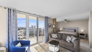 A modern living room with a sofa, a round coffee table, and a view of the city through large sliding glass doors. - Sky High View at EB& Tennis 1002C-NEW LISTING (Fort Myers Beach)