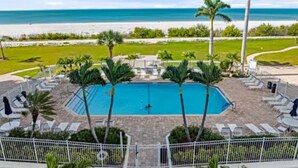 A swimming pool surrounded by palm trees and lounge chairs, with a view of the beach and ocean. - Sunset Views at EB & Tennis Club 104C (Fort Myers Beach)