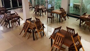 A spacious indoor area with multiple wooden tables and chairs arranged in clusters, large windows allowing natural light, and a tiled floor. - Hotel Viana (Viana)