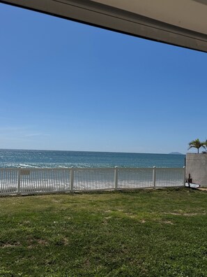 A view of the ocean from a balcony with a white fence and a grassy area in the foreground.