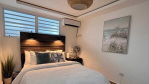 A bedroom with a large bed, a ceiling fan, a wall-mounted air conditioner, and a window with blinds. - Oceanfront Rincón Stay, Amazing Sunsets & Walking distance to many restaurants. (Rincon)