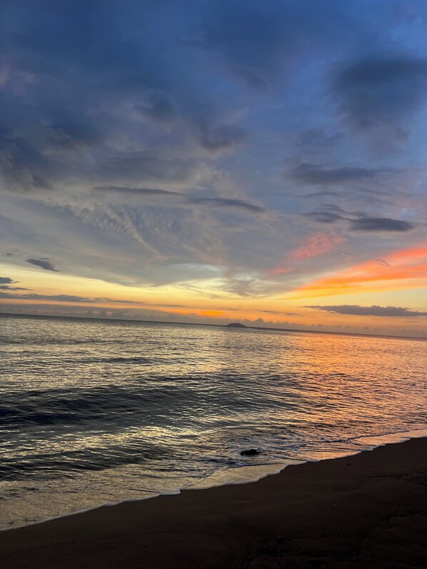 A beach with calm water reflecting the sky during sunset.