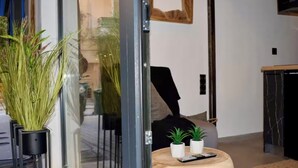 Una sala de estar moderna con un ventanal que da a un comedor, una mesita redonda de madera con un control remoto y dos pequeñas macetas.