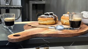Una tabla de madera con un pastel, una taza de café y una rosquilla sobre una mesa.