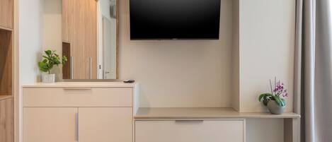 A modern bathroom with a flat-screen TV mounted above a vanity, a mirror, and a potted orchid.
