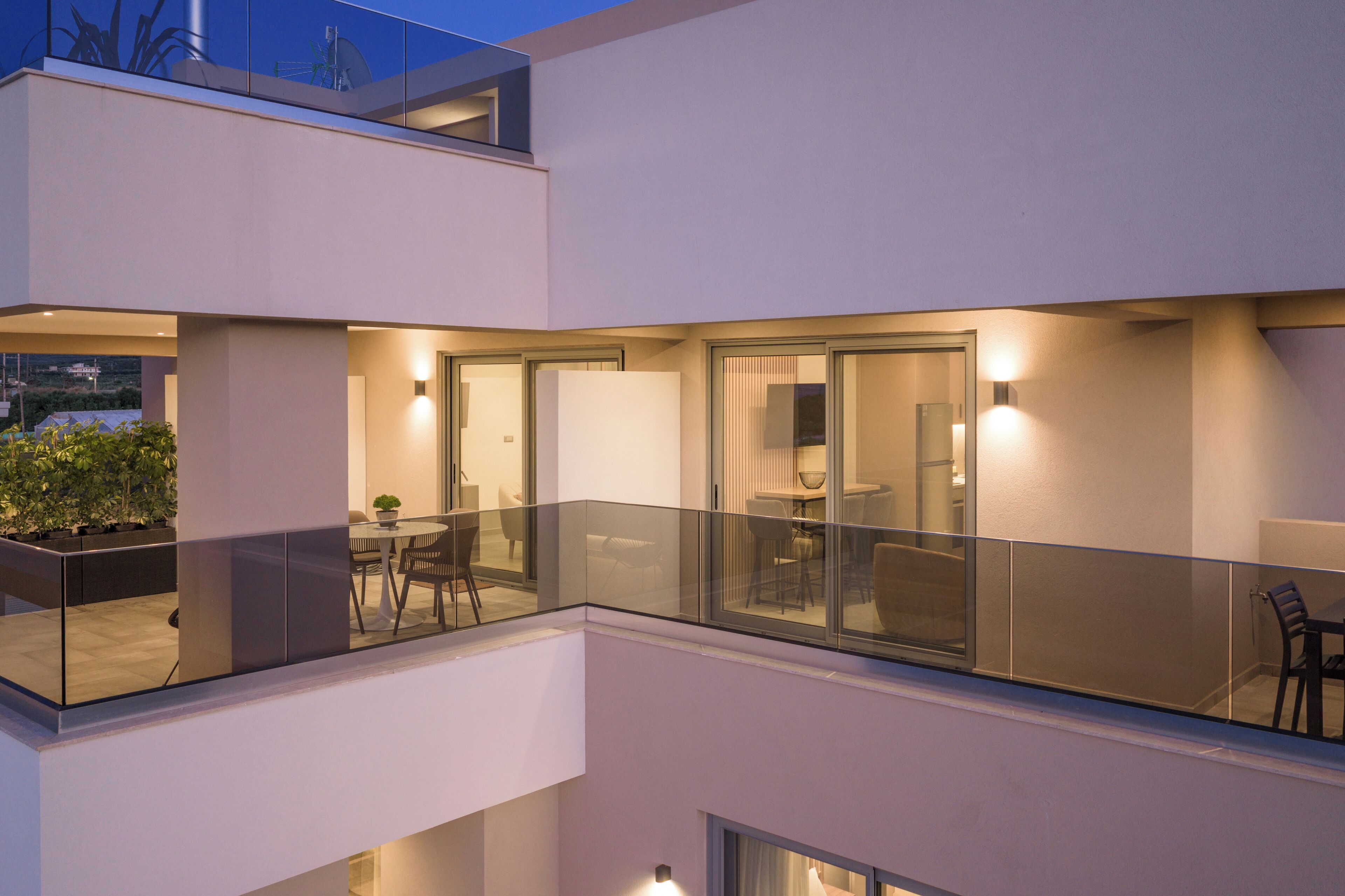A modern multi-level residential building with glass railings, a dining area, and a visible outdoor garden.