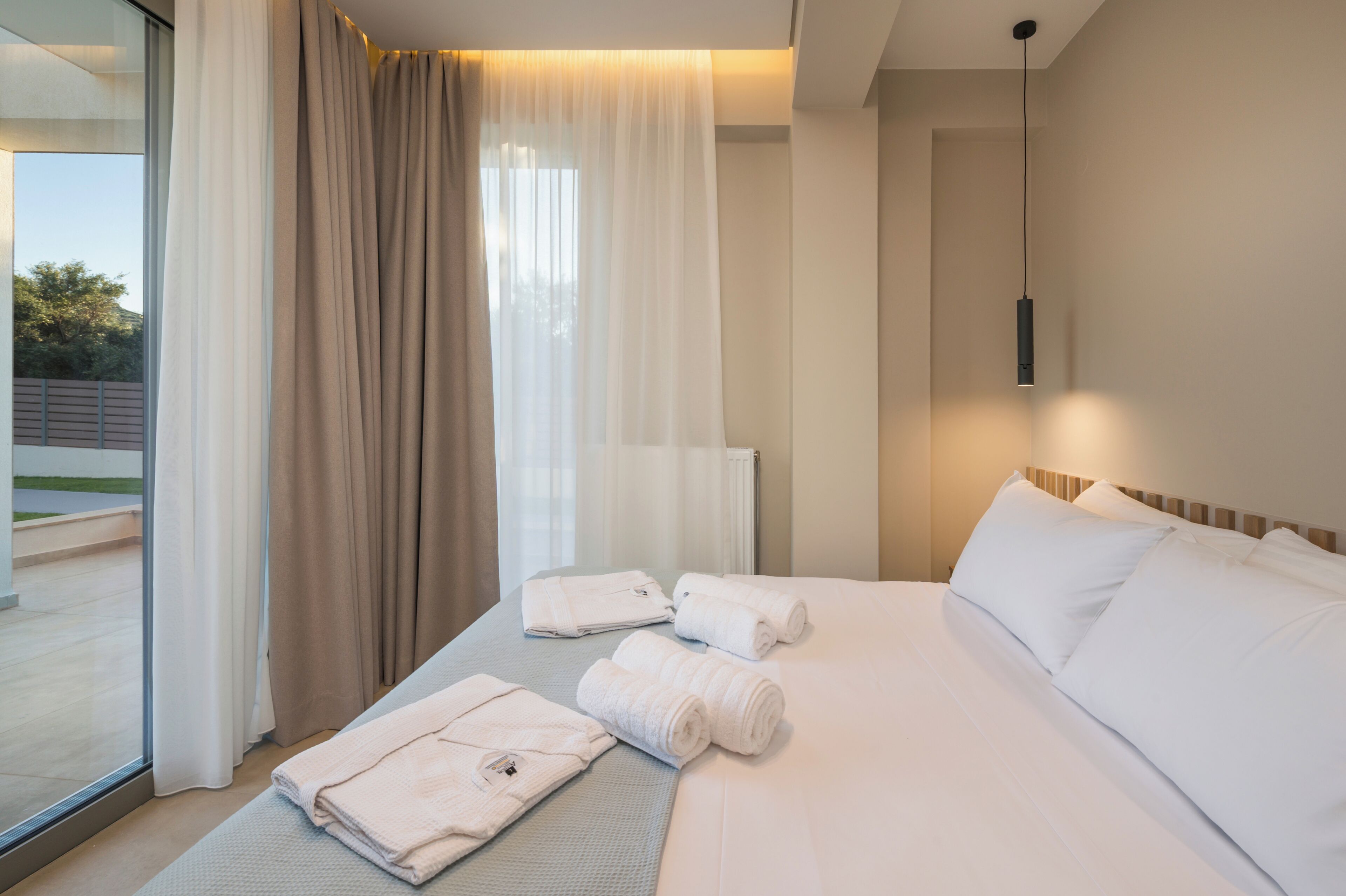 A hotel room with a bed, towels, a window with curtains, and a pendant light.